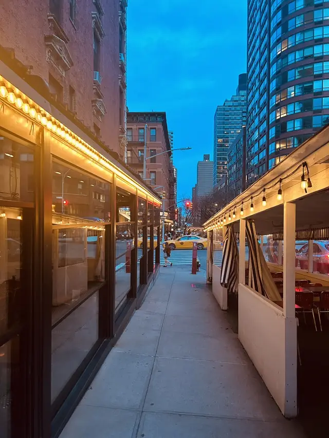 Lit outdoor dining sheds under a blue New York dusk