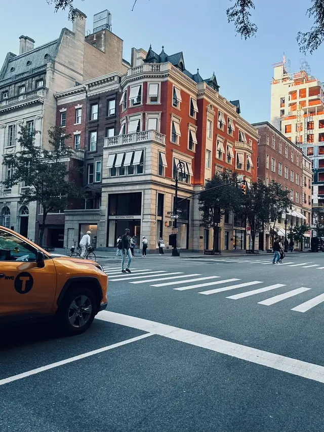 A New York taxi at a crosswalk between brick and limestone corner buildings