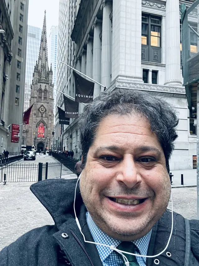 Kareem E. Abdo on Wall Street with the spire of Trinity Church behind him